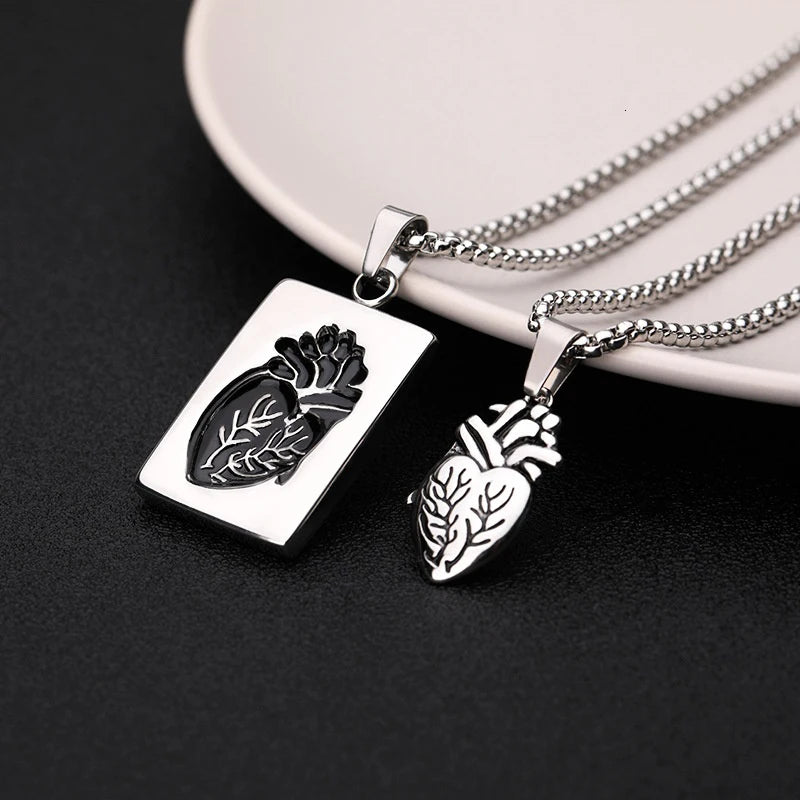 Two silver pendants shaped like anatomical hearts on a dark surface with a white plate in the background.