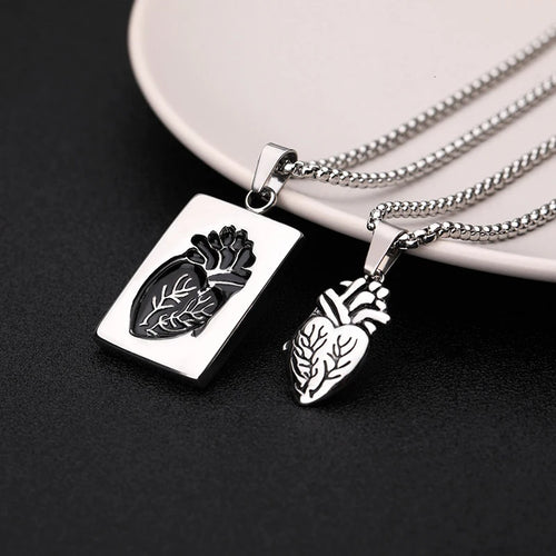 Two silver pendants shaped like anatomical hearts on a dark surface with a white plate in the background.